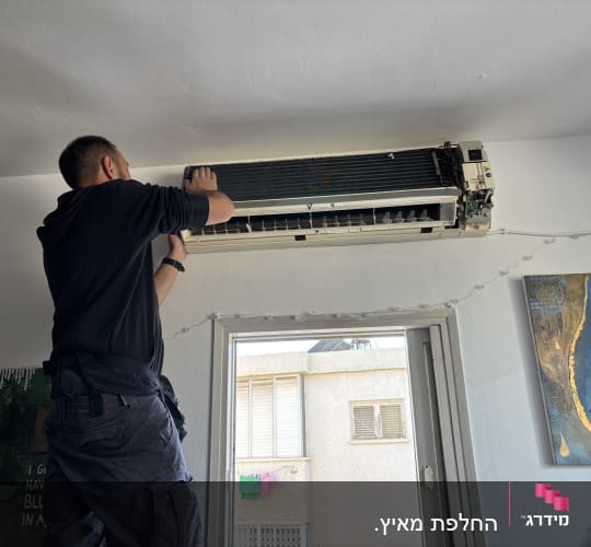 אדם מתקן מזגן על קיר פנימי בחדר.